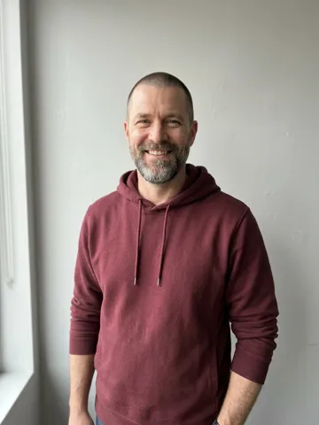 Photo of a bearded man in a maroon hoodie cast on the balcony